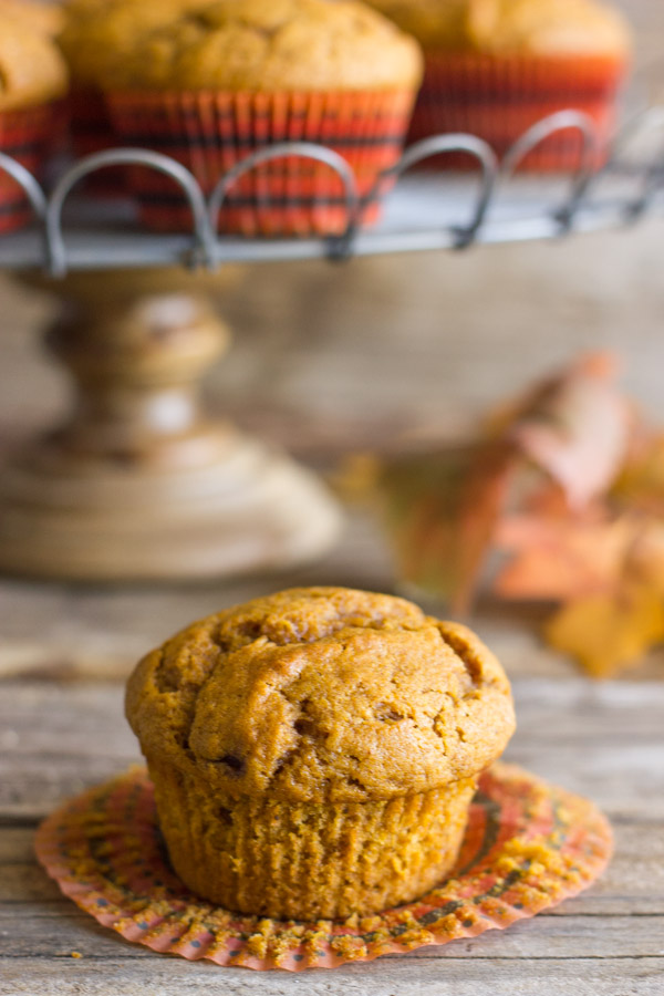 Best Ever Pumpkin Muffin with its wrapper pulled down and more muffins on a metal cake stand in the background.  