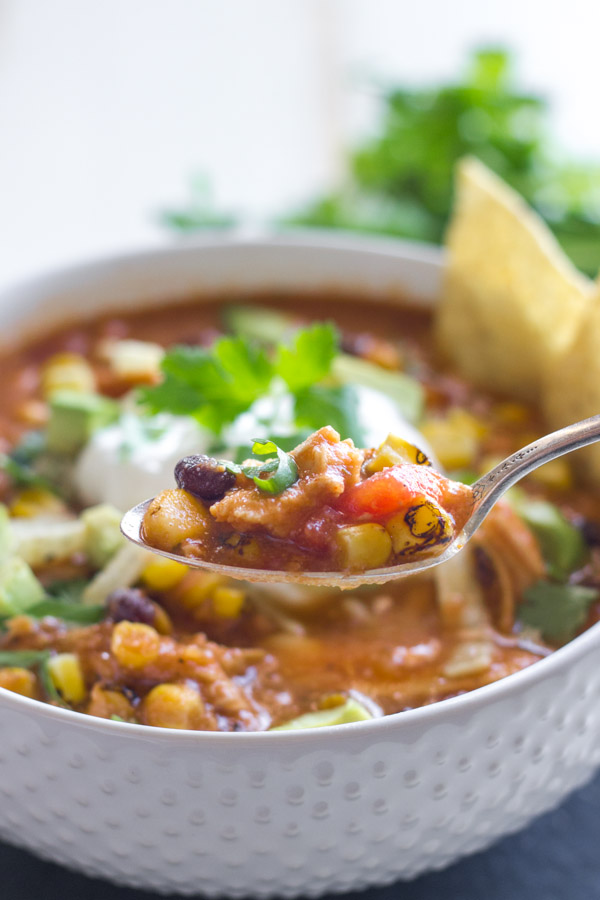 A close up of a spoonful of Crockpot Chicken Tortilla Soup, with a bowl of the soup in the background.  