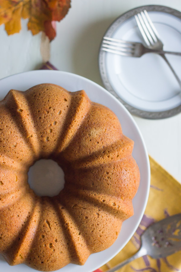 Pumpkin Spice Bundt Cake on a cake stand, with a serving utensil and a plate with forks next to the stand.