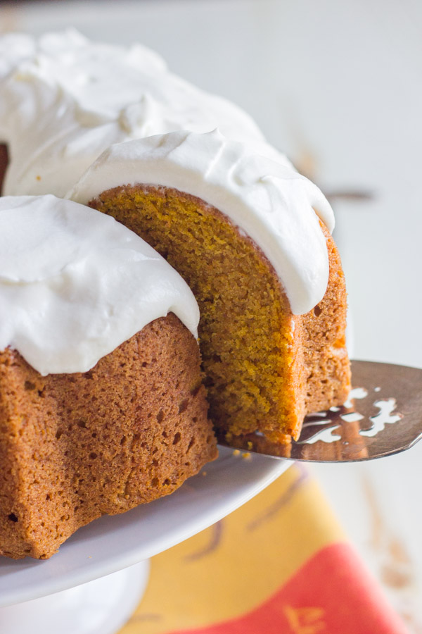A slice of Pumpkin Spice Bundt Cake with frosting on a serving utensil, being pulled away from the rest of the cake.