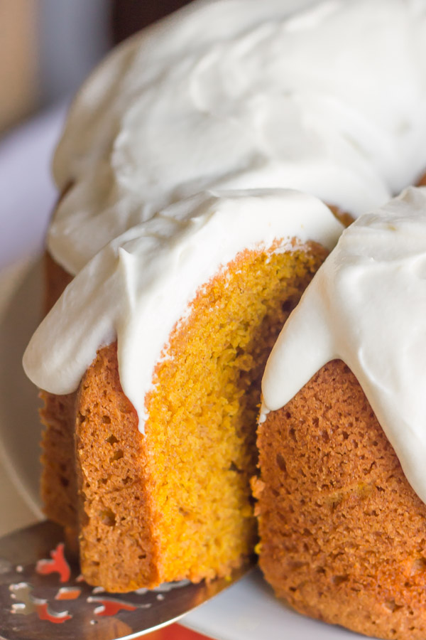 A slice of Pumpkin Spice Bundt Cake with frosting on a serving utensil, being pulled away from the rest of the cake.
