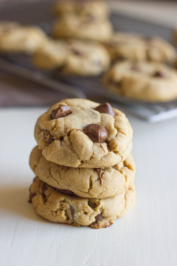 Peanut Butter Cookies With Peanut Butter Filled Chocolate Chips stacked in a pile of three, with more cookies on a cooling rack in the background. 