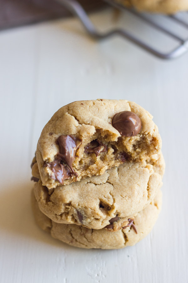 Peanut Butter Cookies With Peanut Butter Filled Chocolate Chips stacked in a pile of three, with the top one being a half of a cookie.  