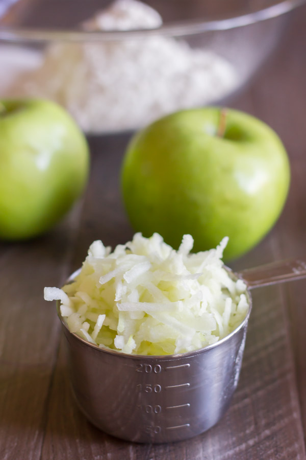 Grated Granny Smith apple in a measuring cup, with whole apples in the background.  