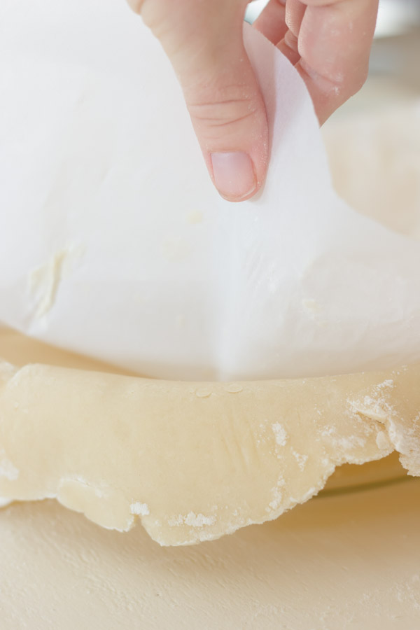 Pie Crust Tutorial Step 6 - parchment paper being peeled away from the pie dough after it was placed in the pie plate.