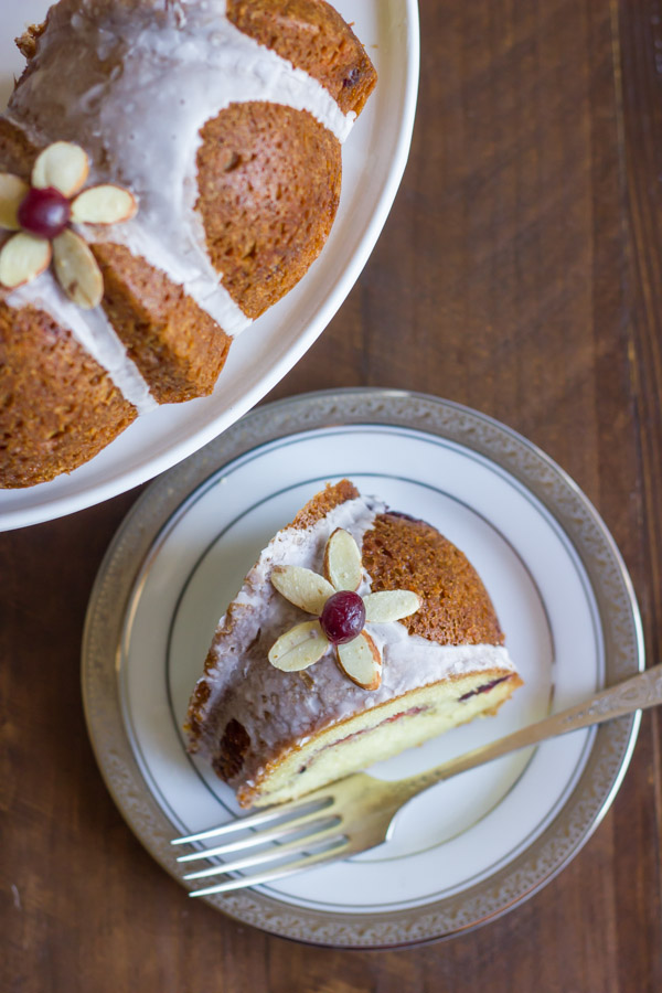 Cranberry Almond Greek Yogurt Cake slice on a plate with a fork, next to the rest of the cake on a cake stand.  