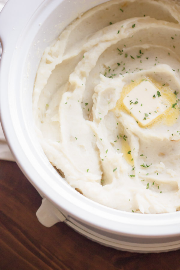 Easy Creamy Crockpot Roasted Garlic Mashed Potatoes in the crockpot, topped with butter and dried parsley.