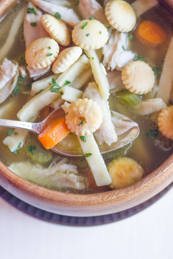 Homemade Chicken Noodle Soup in a bowl with a spoon, topped with oyster crackers.  