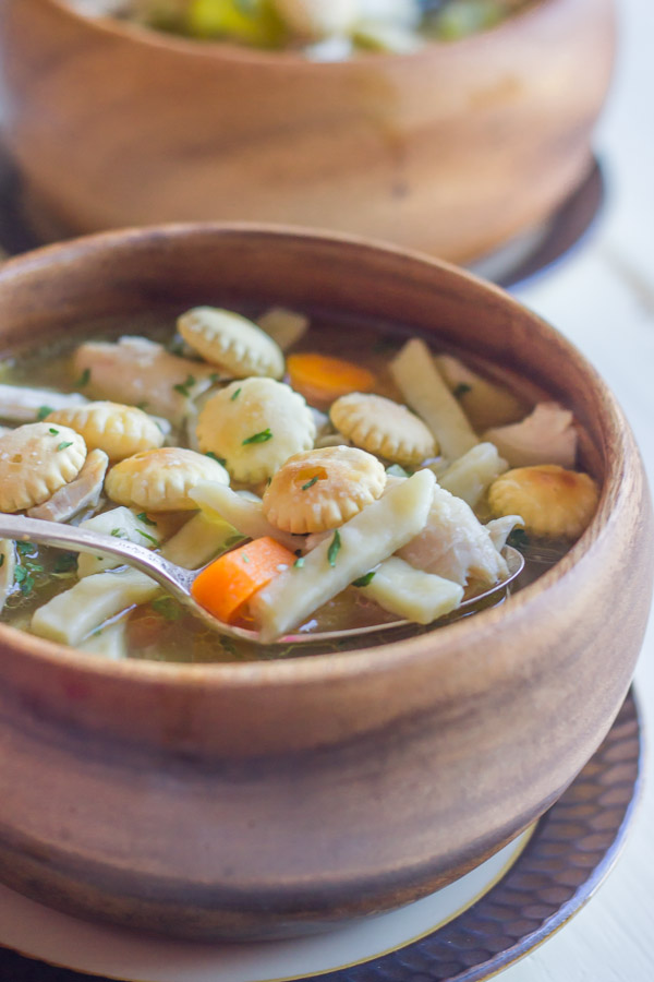 Homemade Chicken Noodle Soup in a bowl with a spoon, topped with oyster crackers.  