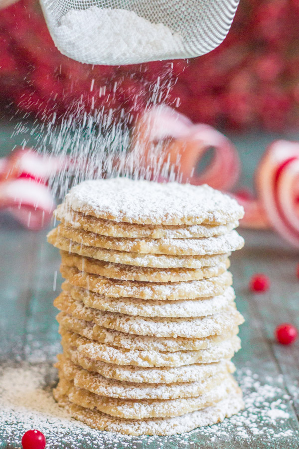 Christmas Oatmeal Cookies stacked in a pile, being dusted with powdered sugar.