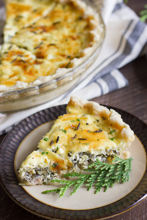 Cheesy Wild Rice Quiche slice on a plate, with the rest of the quiche in a pie plate in the background.