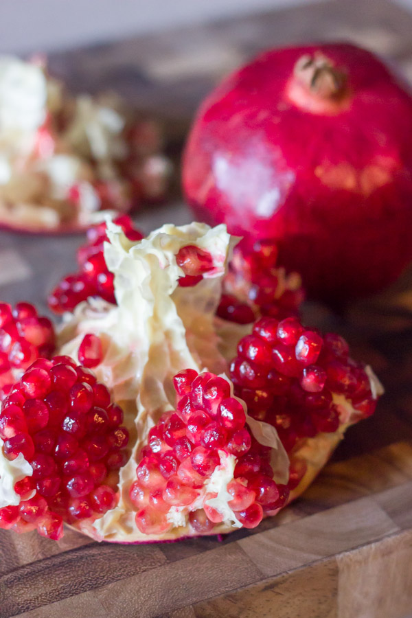 A pomegranate cut open on a cutting board, sitting next to a whole pomegranate.  