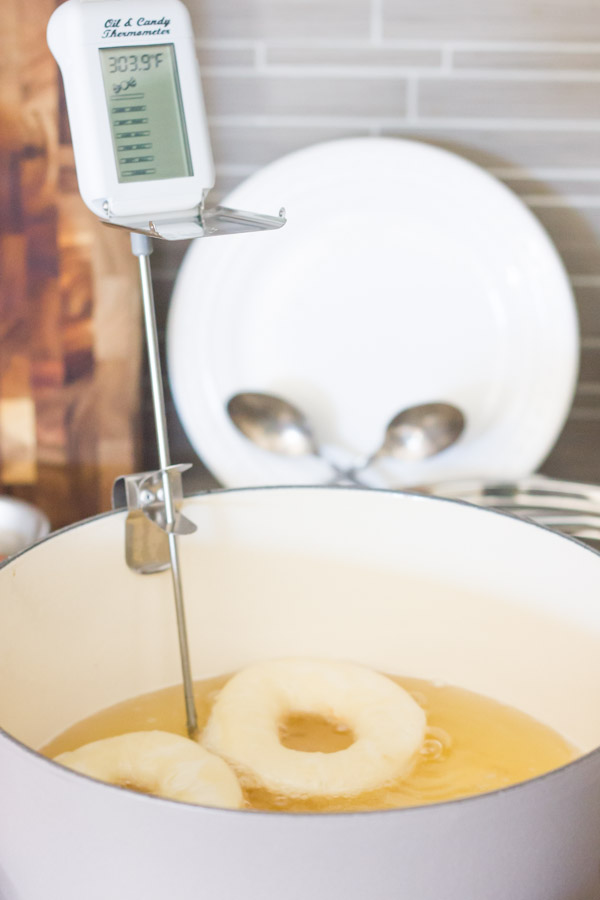 A large pot with a thermometer on it, with oil inside and two donuts frying in it.