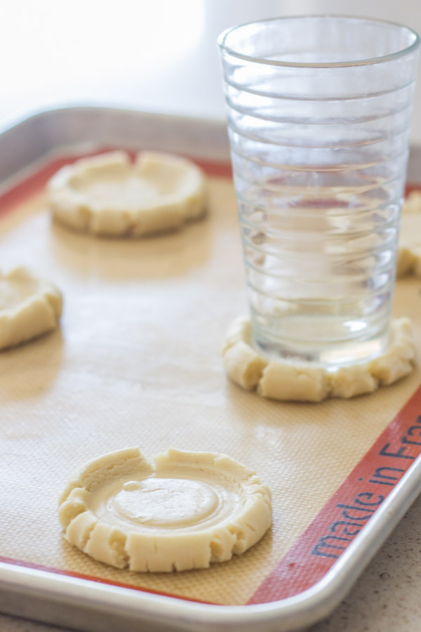 Swig Style Frosted Sugar Cookie smashed dough on a Silpat lined baking sheet, with a glass cup on top of one of them.