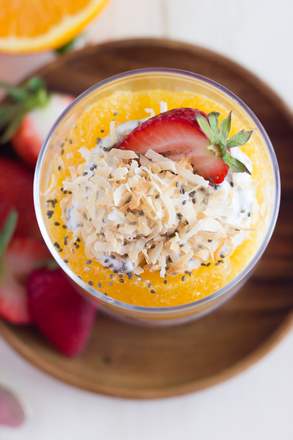 Toasted Coconut Chia Yogurt Fruit Parfait in a glass cup, sitting on a wood plate with strawberry slices.  