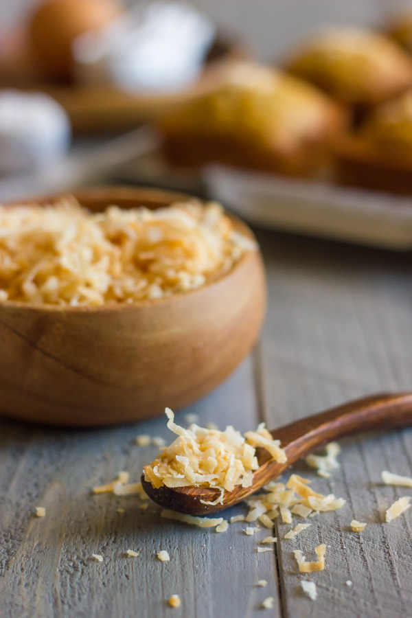 A small spoon full of Toasted Coconut, with a bowl full of Toast Coconut behind it.  