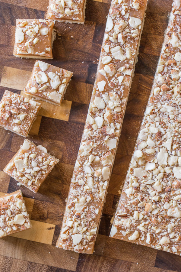Homemade Caramel Almond Shortbread Bites being cut into squares on a cutting board.