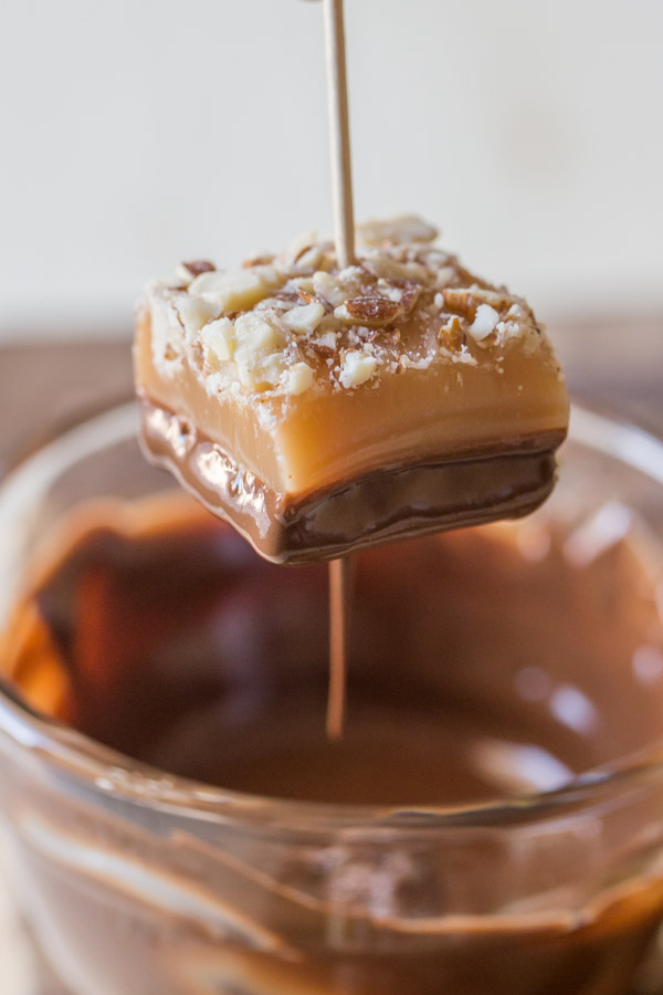 Homemade Caramel Almond Shortbread Bite with a toothpick in it, that has just been dipped into the melted chocolate.