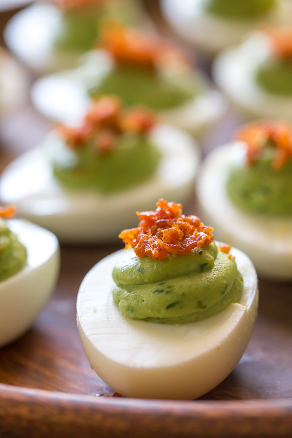 Smoky Bacon Avocado Deviled Eggs arranged on a wood plate.  