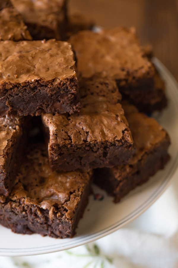 Extra Thick Fudgy Homemade Brownies cut in squares and stacked on a cake stand. 