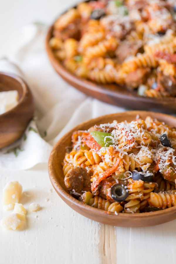Supreme Pizza Pasta in a wood bowl topped with parmesan cheese, with the serving dish of pasta in the background.  