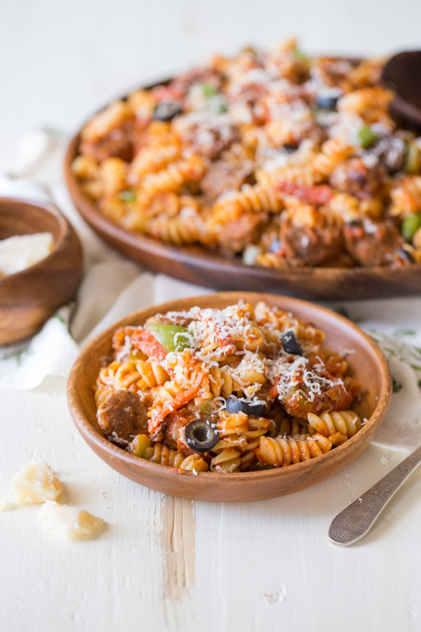 Supreme Pizza Pasta in a wood bowl topped with parmesan cheese, with the serving dish of pasta in the background.  