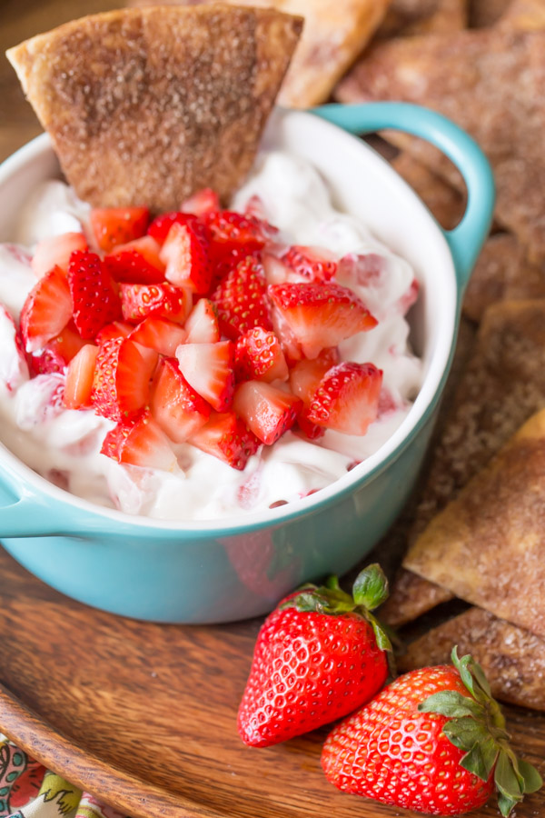 Baked Cinnamon Crisps on a wood plate with a bowl of Creamy Strawberry Dip and a few whole strawberries.  