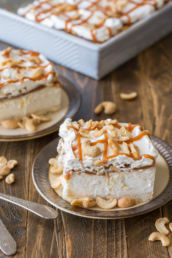Two Caramel Cashew Ice Cream Dessert square servings on plates, with the rest of the pan of dessert in the background.
