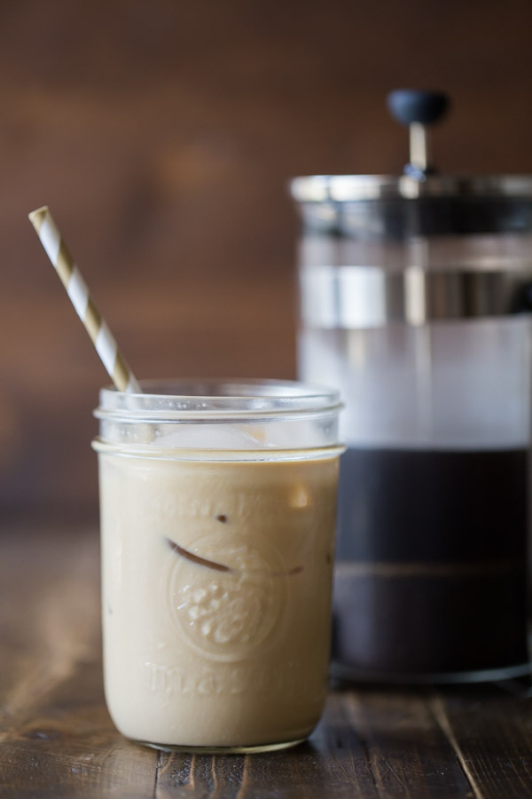 Cold Brew Iced Coffee mixed with some Homemade Vanilla Creamer in a glass jar with a straw, and a French press in the background.  