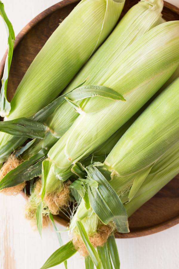 A pile of Corn on the Cob with the husks still on.  