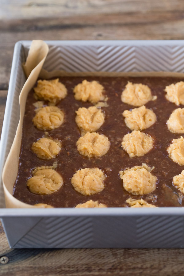 Homemade brownie batter studded with globs of peanut butter cookie dough in a parchment paper lined baking pan.