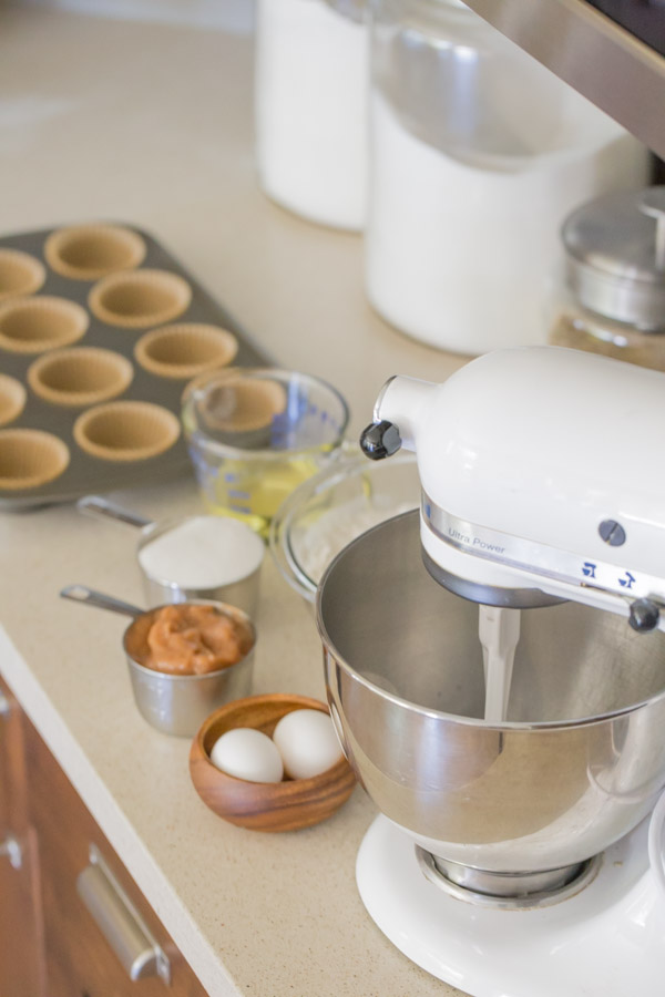 Ingredients for the Apple Cupcakes With Dulce De Leche Buttercream sitting on the counter next to an electric mixer and a lined muffin pan.  