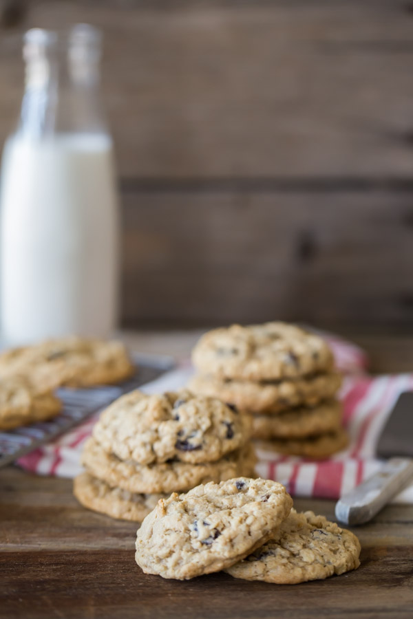 Pumpkin Pie Spice Oatmeal Raisin Cookies in stacks, with a glass container of milk in the background.  