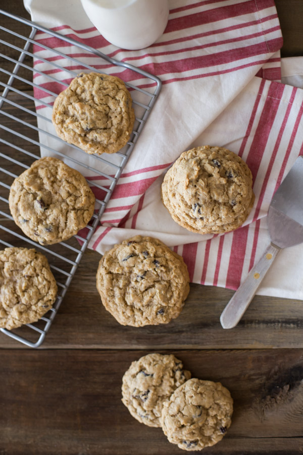 Pumpkin Pie Spice Oatmeal Raisin Cookies on a cooling rack and next to it, along with a glass of milk and a spatula.  