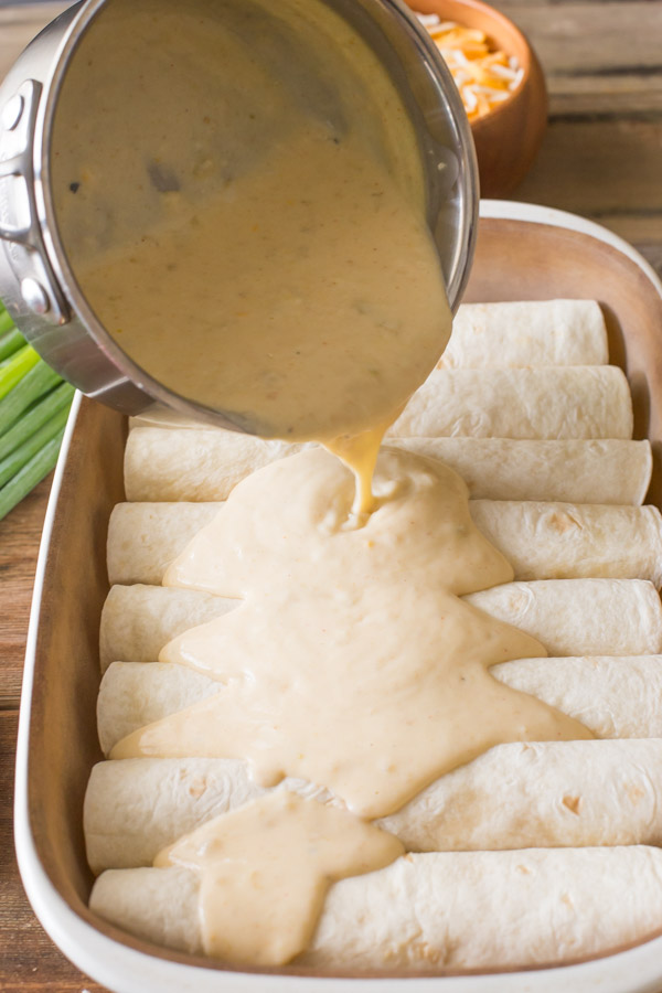 The creamy cheese sauce being poured over the stuffed, rolled tortillas in the baking dish for the Breakfast Enchilada Bake.