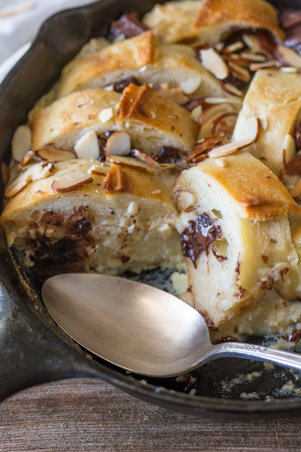 Chocolate Almond Bread Pudding in a cast iron skillet with a spoon, and some of the bread pudding gone.  