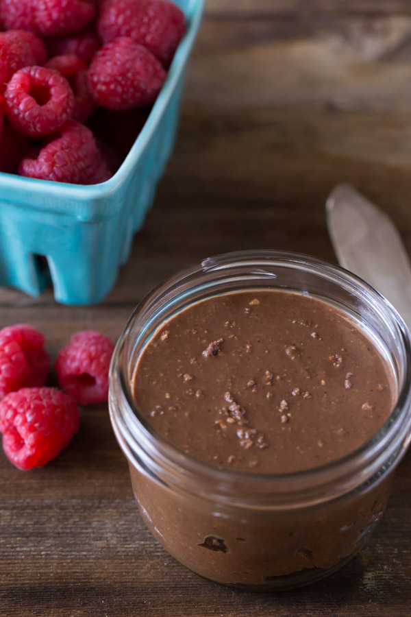 A glass jar of Chocolate Hazelnut Butter, next to a carton of raspberries.