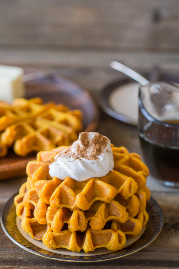 Pumpkin Spice Waffles stacked on a plate, topped with whipped cream and cinnamon.