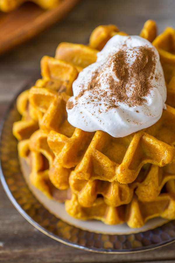 Pumpkin Spice Waffles stacked on a plate, topped with whipped cream and cinnamon.