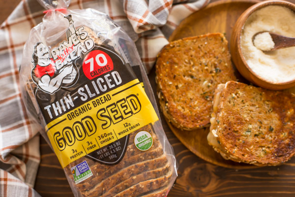 Garlic Bread Toasted Cheese Sandwiches on a wood plate along with a small wood bowl of grated Parmesan cheese, with a bag of Dave's Killer Bread next to it.