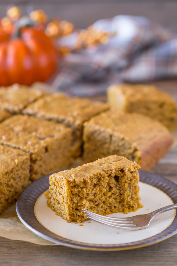A half eaten piece of Healthier Pumpkin Spice Snack Cake on a plate with a fork, with the rest of the cut cake in the the background.  