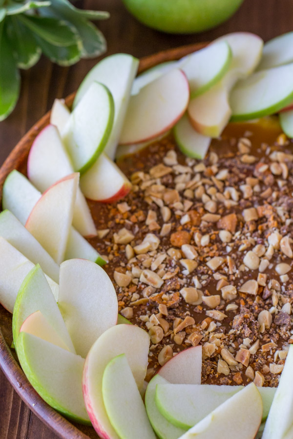 Easy Caramel Apple Dip on a wood plate with sliced apples arranged around it.