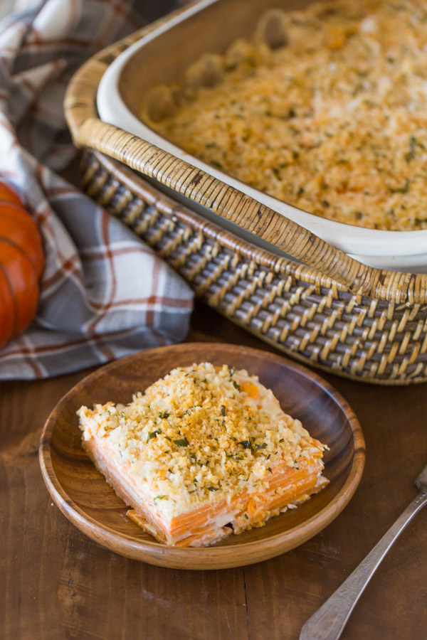 A serving of Smoked Chili Sweet Potato Gratin on a wood plate, with the baking dish of Smoked Chili Sweet Potato Gratin in the background.  