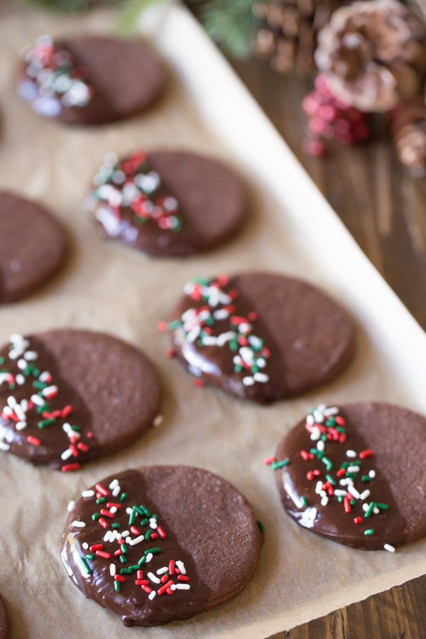 Chocolate Cut-Out Cookies that have been half dipped in melted chocolate and covered with sprinkles.