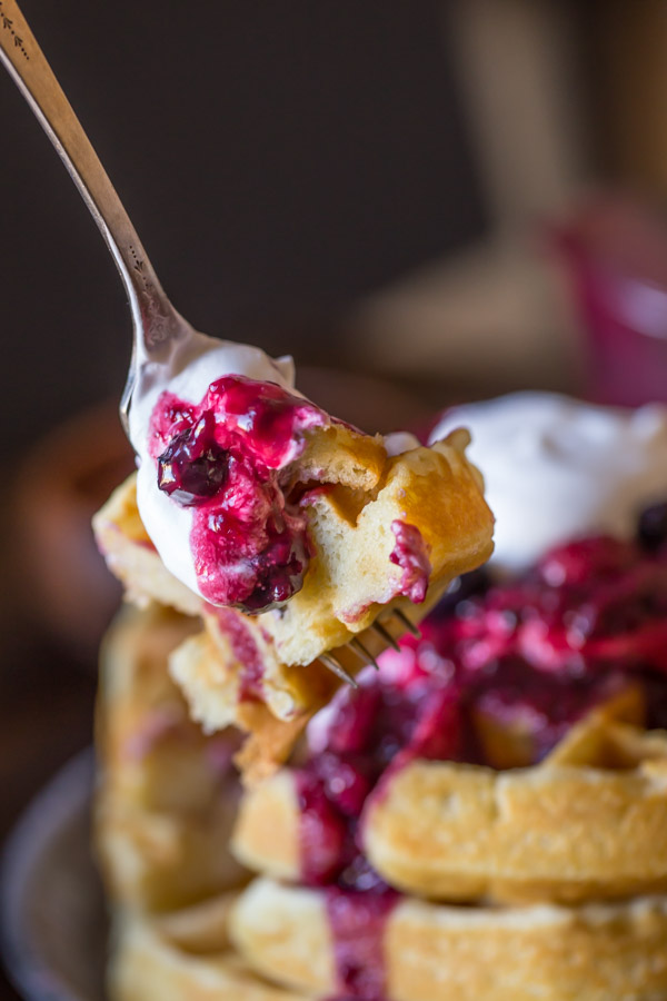 A fork full of the Best Ever Buttermilk Waffles topped with berry sauce, whole berries and whipped cream.  