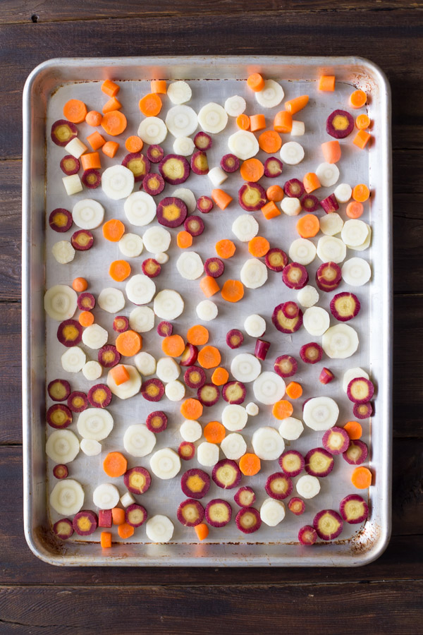Purple, white and orange carrot slices on a baking sheet before roasting.