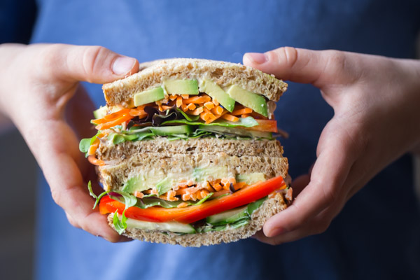 Power Veggie Sandwich - A colorful and power packed sandwich with a generous smear of roasted garlic hummus, and a pile of avocado, cucumber, red pepper, carrots and micro greens.
