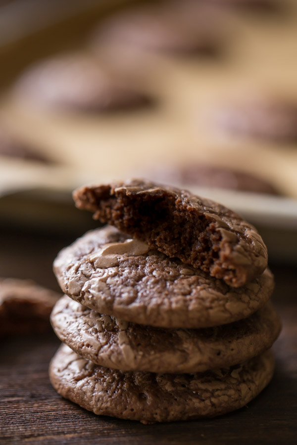 A stack of three Soft and Chewy Brownie Cookies with a half of a cookie on top, and more cookies on a parchment paper lined baking sheet in the background.
