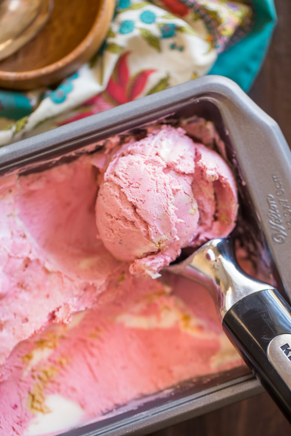 Homemade Raspberry Cheesecake Ice Cream in a loaf pan with an ice cream scoop in it.  
