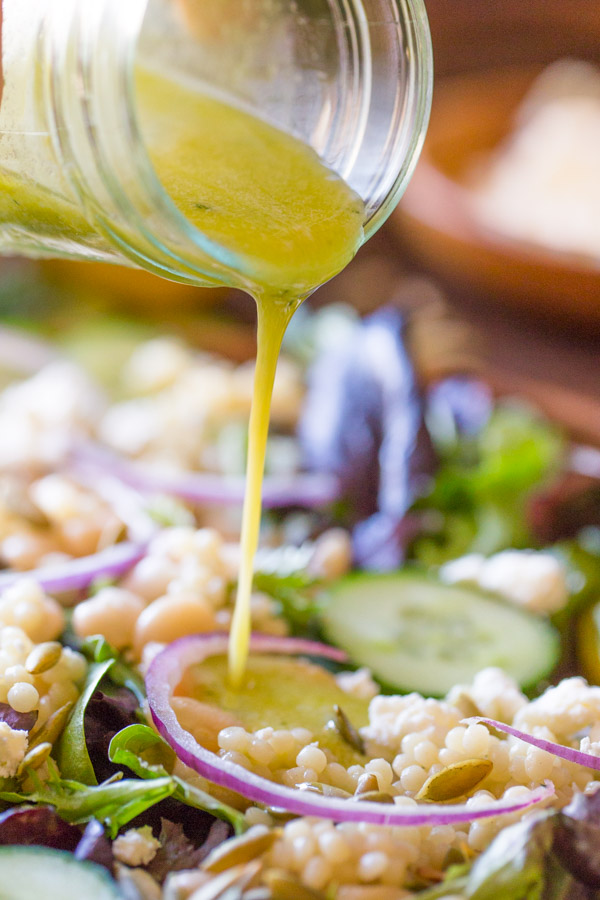 A glass jar of Lemon Vinaigrette being poured on top of the White Bean Couscous Salad.